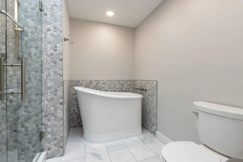 Freestanding tub and toilet beside the glass shower panel on white floor tile