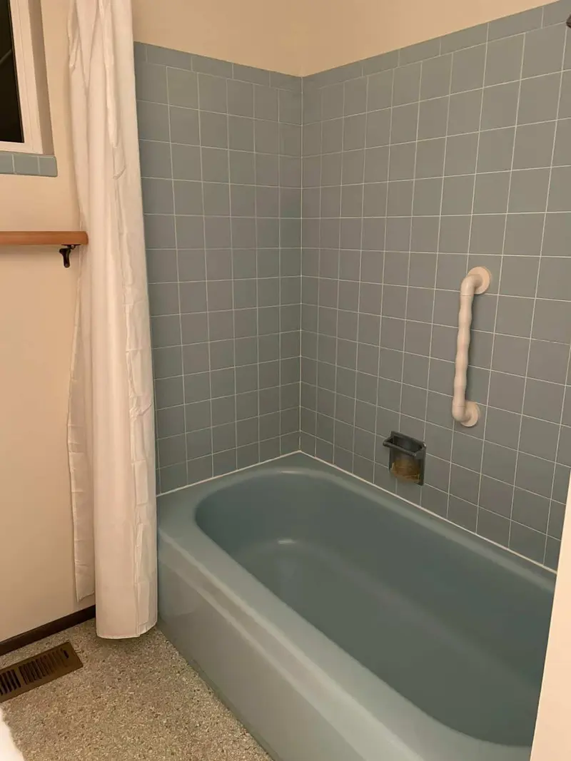 Original blue bathtub with blue square tile and a grab bar