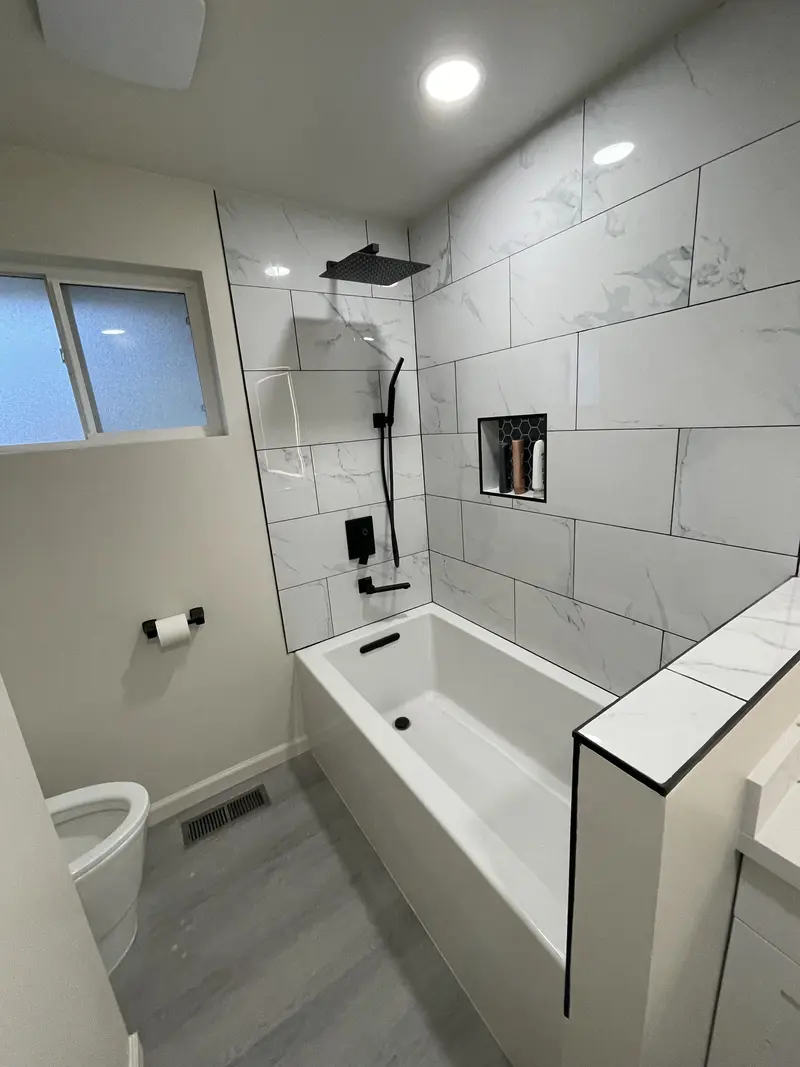 Soaking tub with a tiled ledge, black rain shower and large-format marble-look wall tile