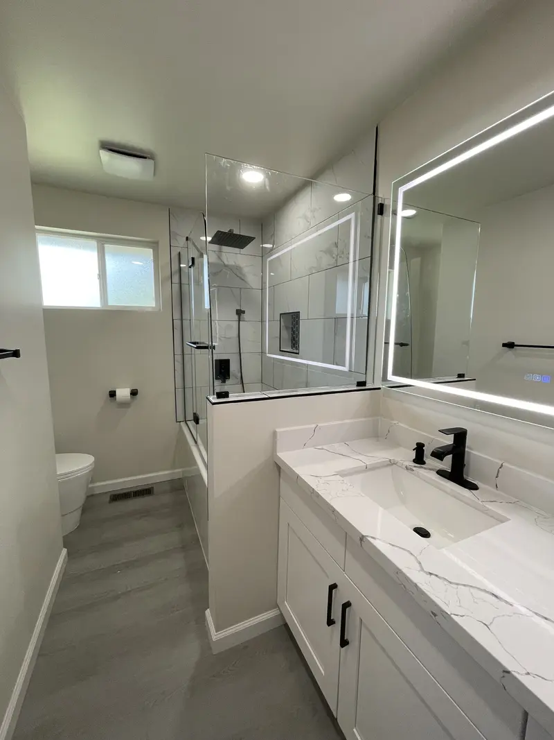 Bathroom with a glass panel added above the tub half wall and the lit mirror on the right