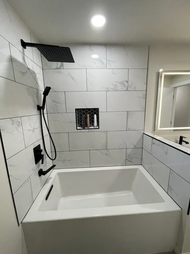 Tub wall with a square black rain shower head, hand shower and two tiled niches