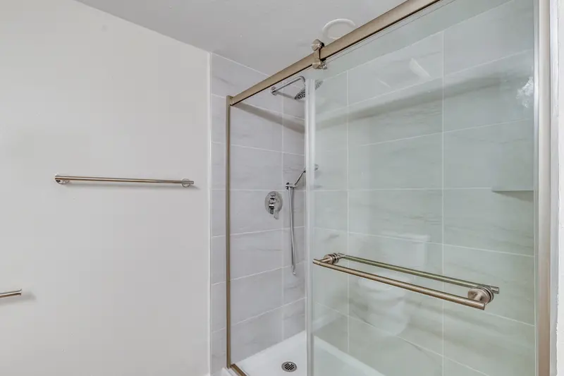 Tiled shower with a sliding glass door, brushed nickel handle and a towel bar beside it