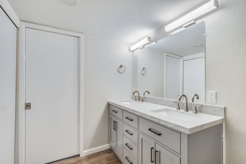 Vanity wall with a gray shaker cabinet, white counter, mirror and light bar beside the bathroom door