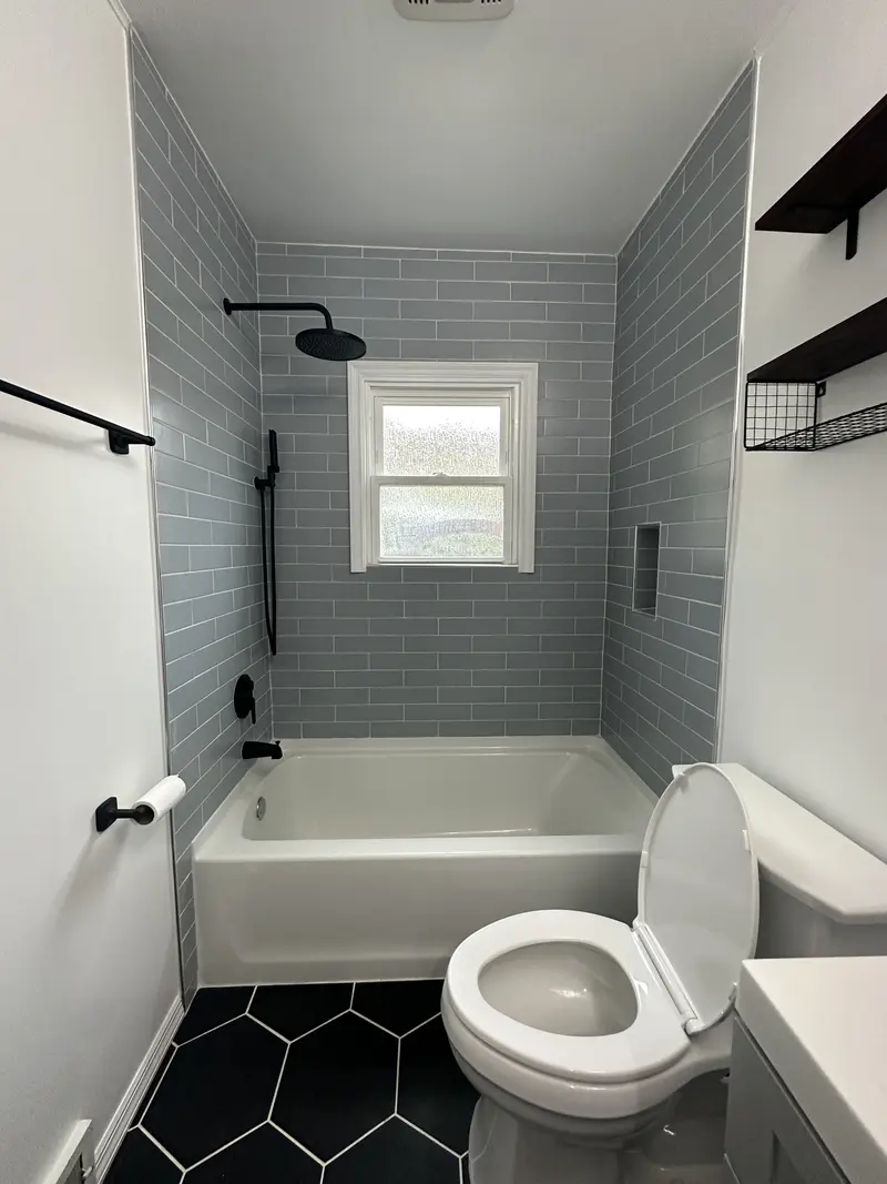 Bathroom window wall with two black metal floating shelves above the toilet