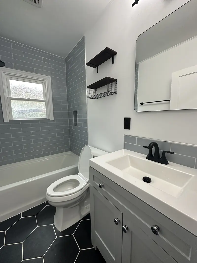 Black hexagon floor tile running from the vanity to the toilet and tub