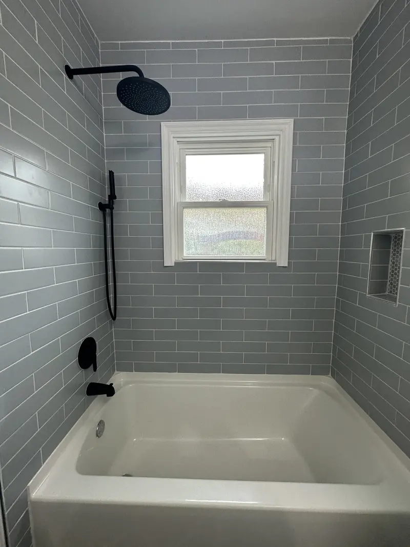 Tub and shower with gray subway tile, a round black rain head, slide bar and a recessed niche under a window