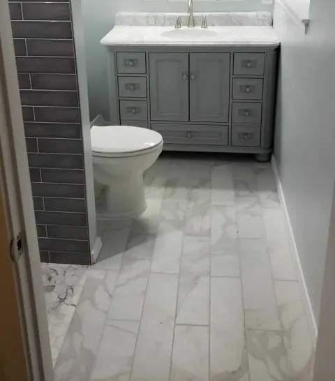 Remodeled bathroom with a gray vanity, white marble top, charcoal tile wall and marble-look floor