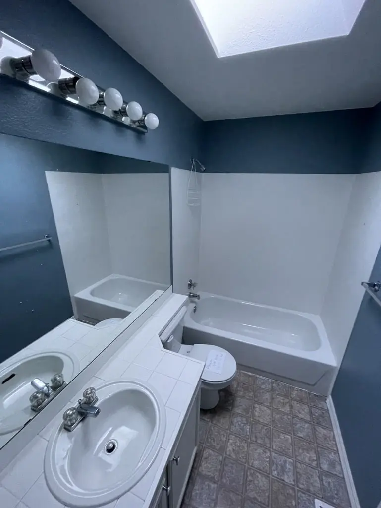 Bathroom before the remodel with dark blue walls, a white molded tub surround, a tile counter and a patterned floor