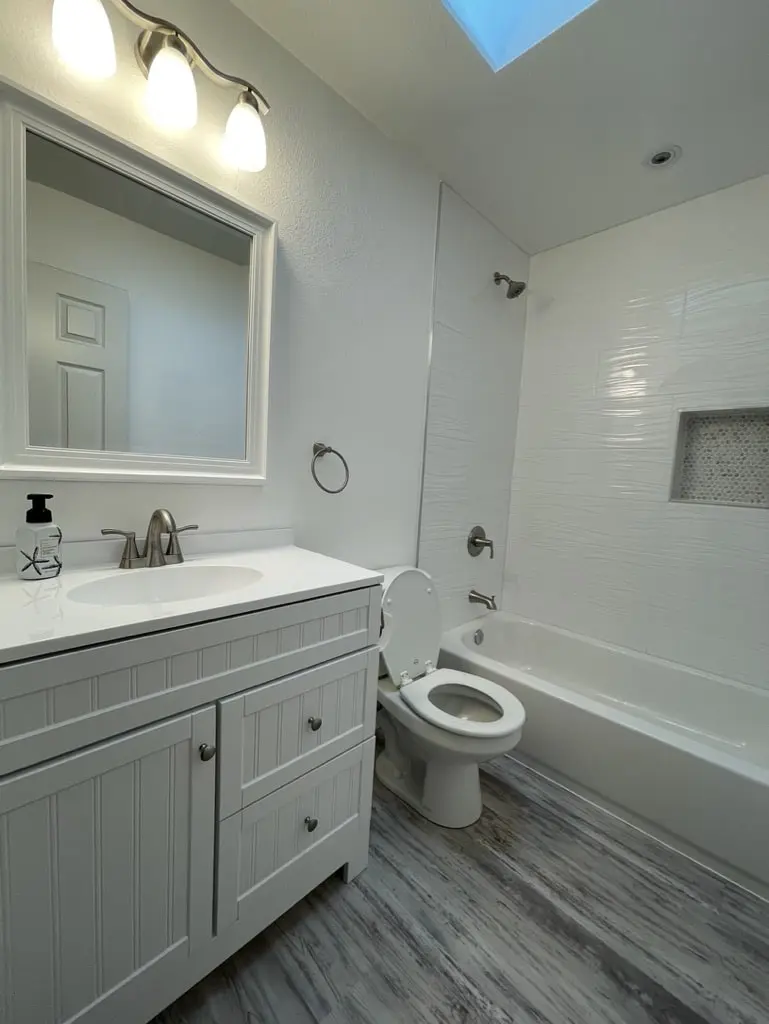 Gray shaker vanity with a white top and brushed nickel faucet beside the toilet and the tile tub surround