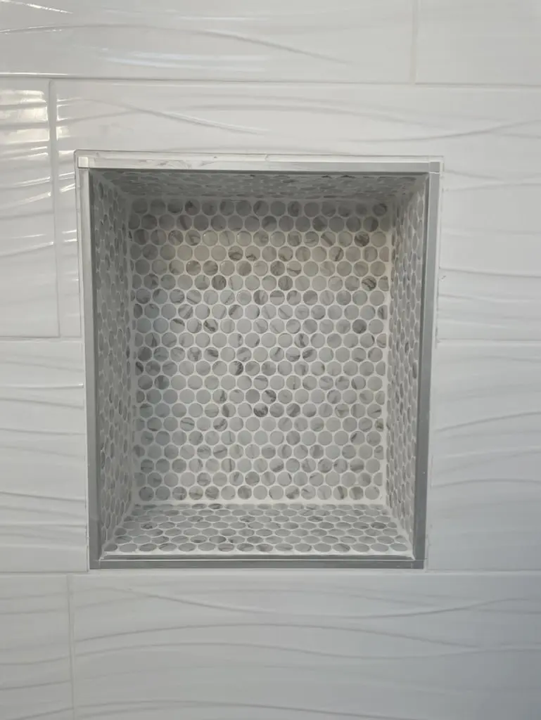 Close view of the recessed niche lined in a gray and white hexagon mosaic within white wave tile