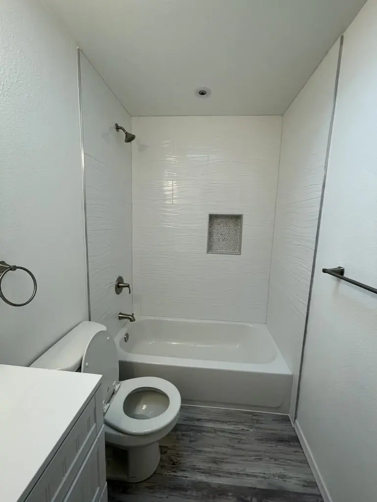 Tub alcove in white wave tile beside the toilet, with a towel ring and towel bar