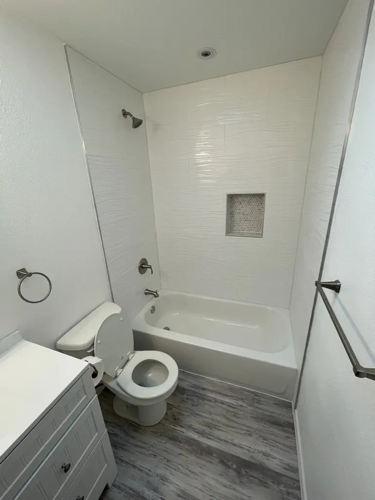 White wave pattern tile tub surround with a recessed niche and a gray plank floor