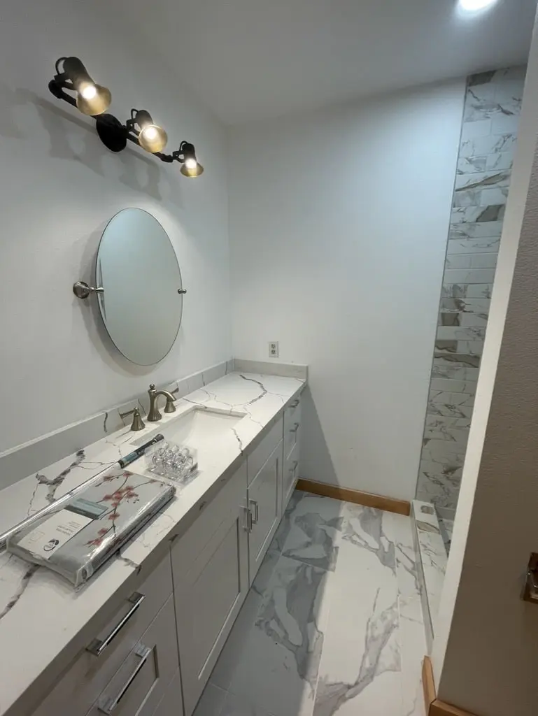 Gray shaker vanity with a round mirror and a black and brass light bar