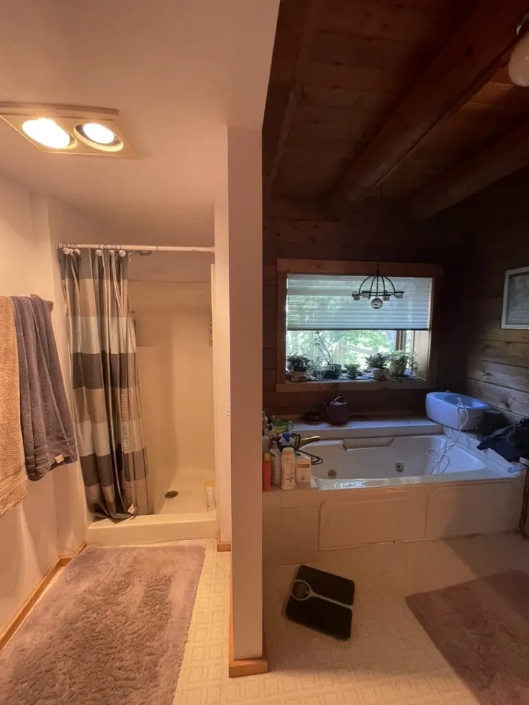 Built-in jetted tub under a window in a log-walled bathroom with a curtained shower beside it