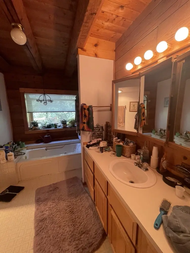 Log home bathroom before the remodel with an oak vanity, globe lights and a jetted tub under the window