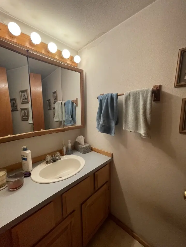 Oak vanity with a cultured marble top and a mirror with globe lights before the remodel