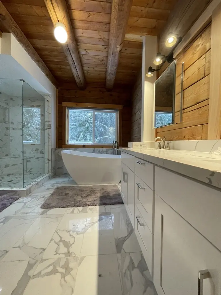 Gray vanity and glass shower in a bathroom with log walls and exposed beams