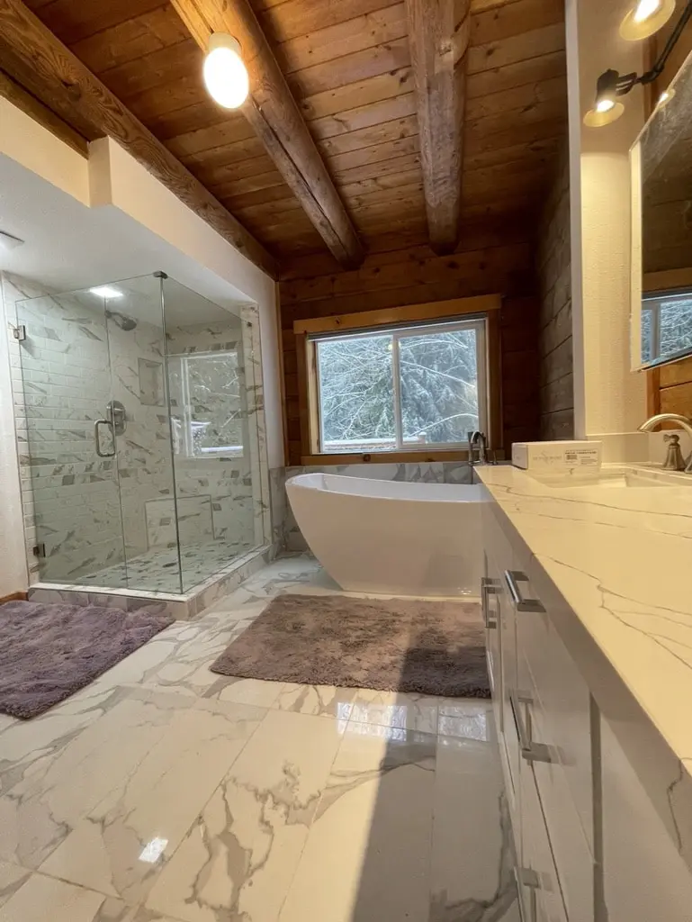 Long gray vanity with a veined white top beside a freestanding tub on a marble-look floor