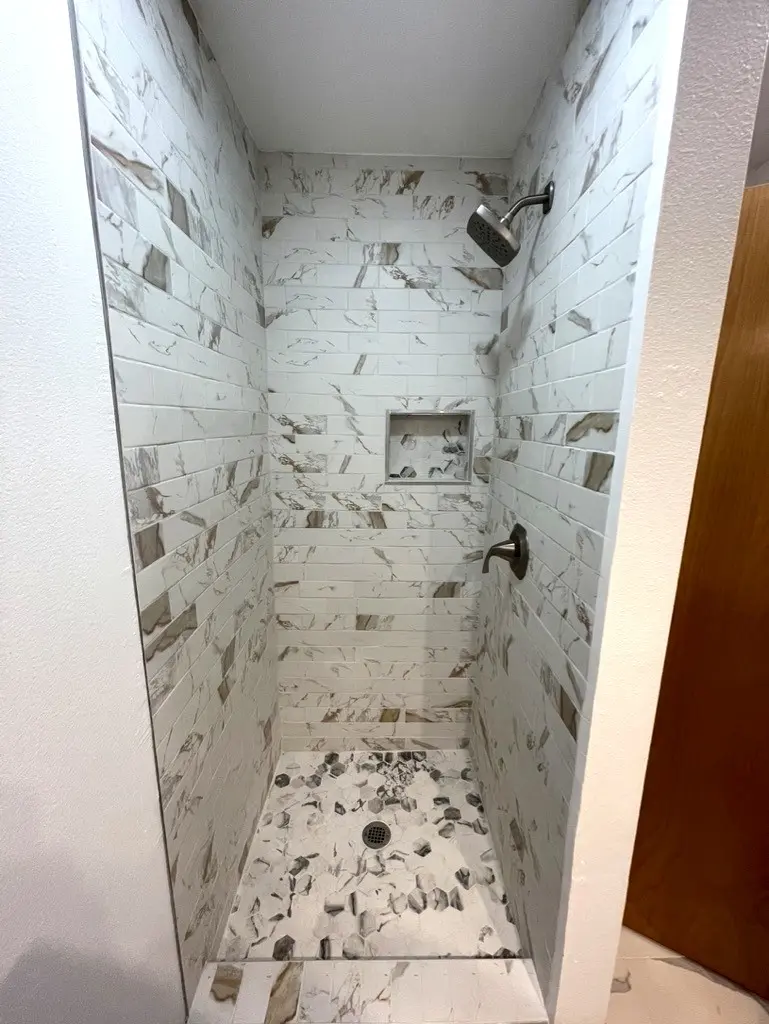 Walk-in shower tiled to the ceiling in white and gray marble-look tile with a recessed niche and a dark shower head