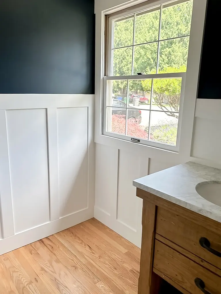 White board and batten wainscoting under a window with navy wall above
