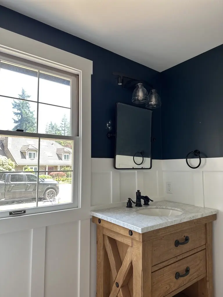 Side view of the wood vanity with an X-brace side and an open lower shelf under a black mirror