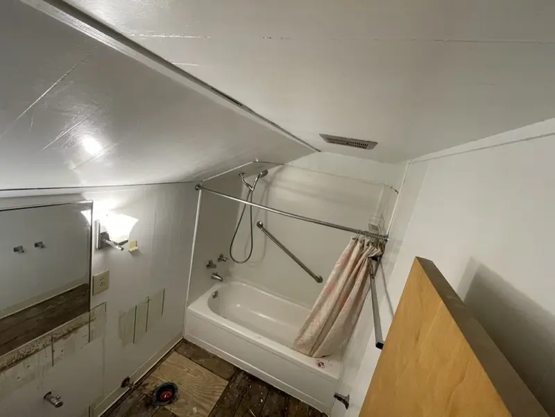Attic bathroom before the remodel with a tub and curtain rod under a sloped ceiling and a dark wood-look floor