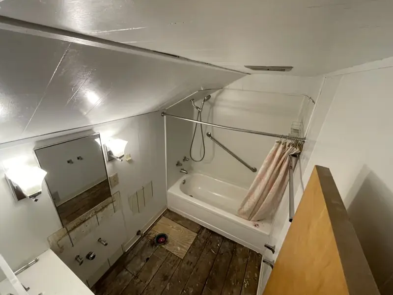 Old vanity mirror and wall light beside a tub under a steep sloped ceiling