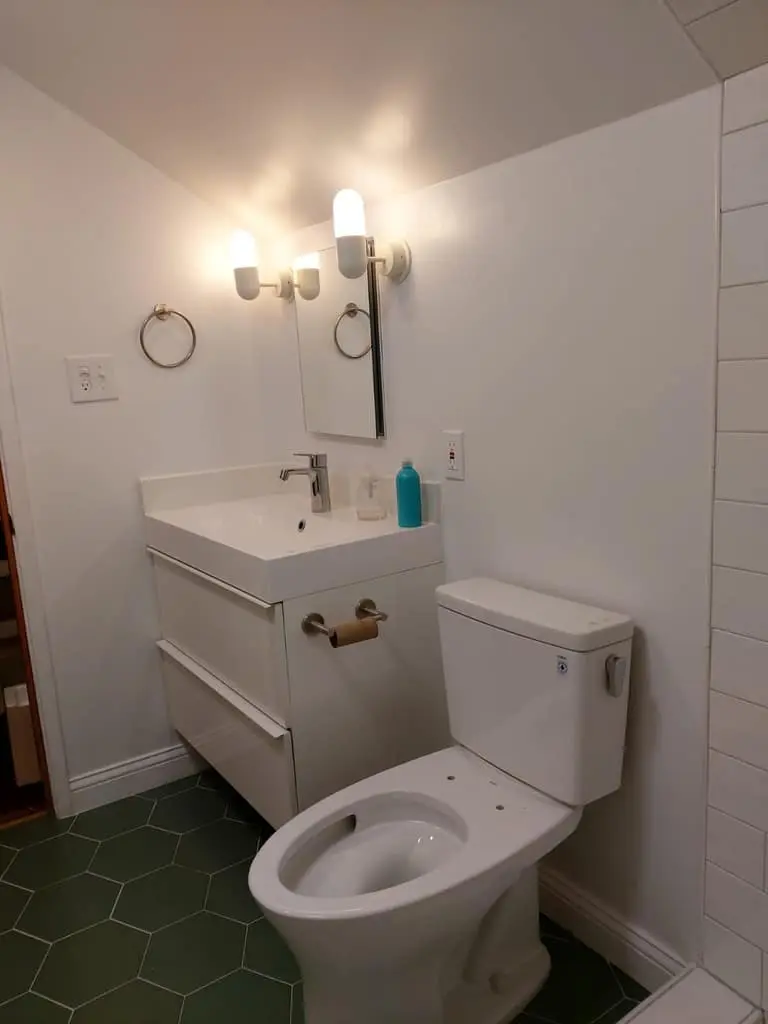 White floating vanity with two wall sconces and a mirror over a green hexagon tile floor