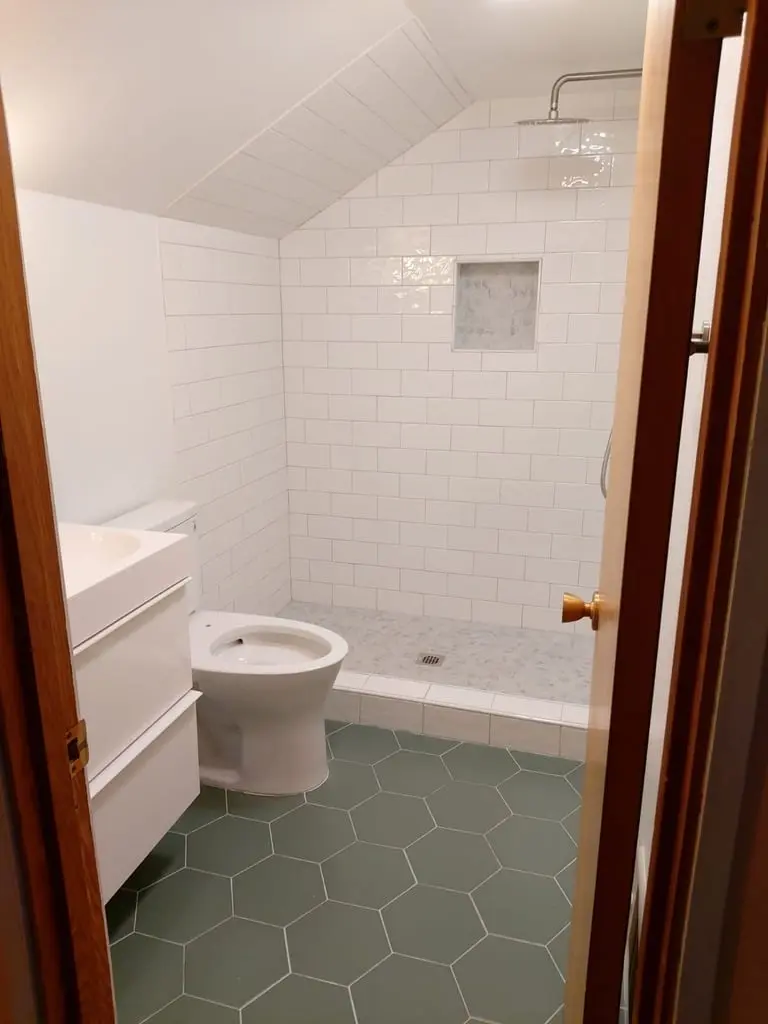 Floating vanity and toilet beside the doorway to a subway tile shower