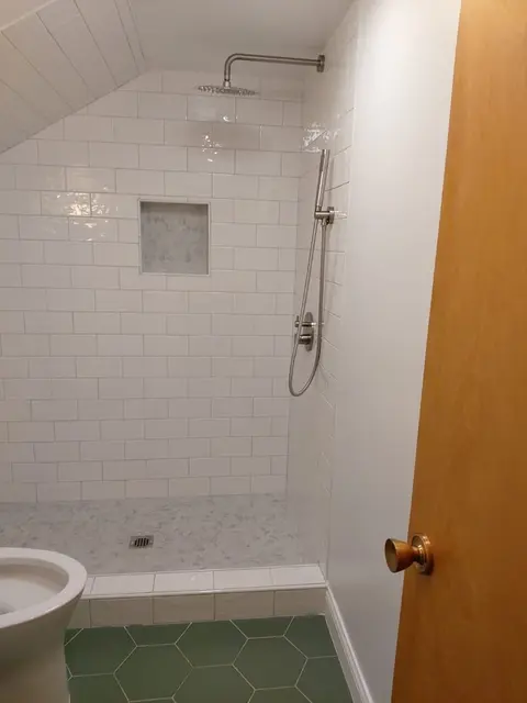 Walk-in shower with white subway tile, a recessed niche and a rain head under a sloped ceiling, green hexagon floor in front
