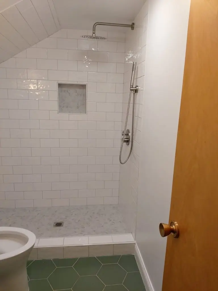 Walk-in shower with white subway tile, a recessed niche and a rain head under a sloped ceiling, green hexagon floor in front
