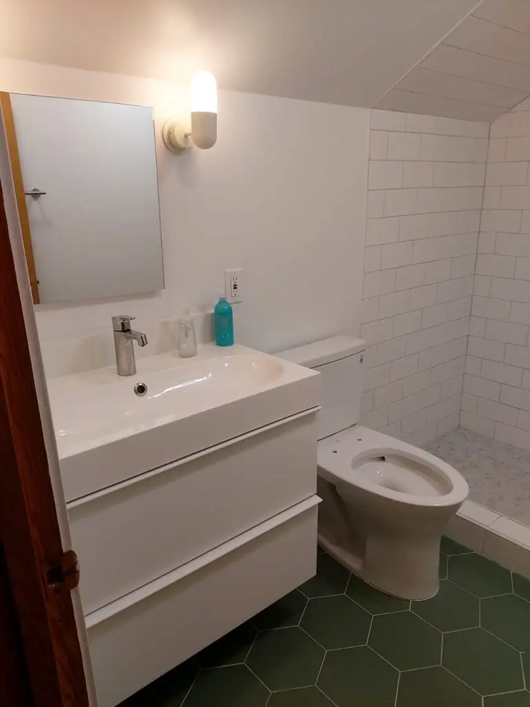 White vanity with a rectangular mirror and wall sconce under a sloped ceiling