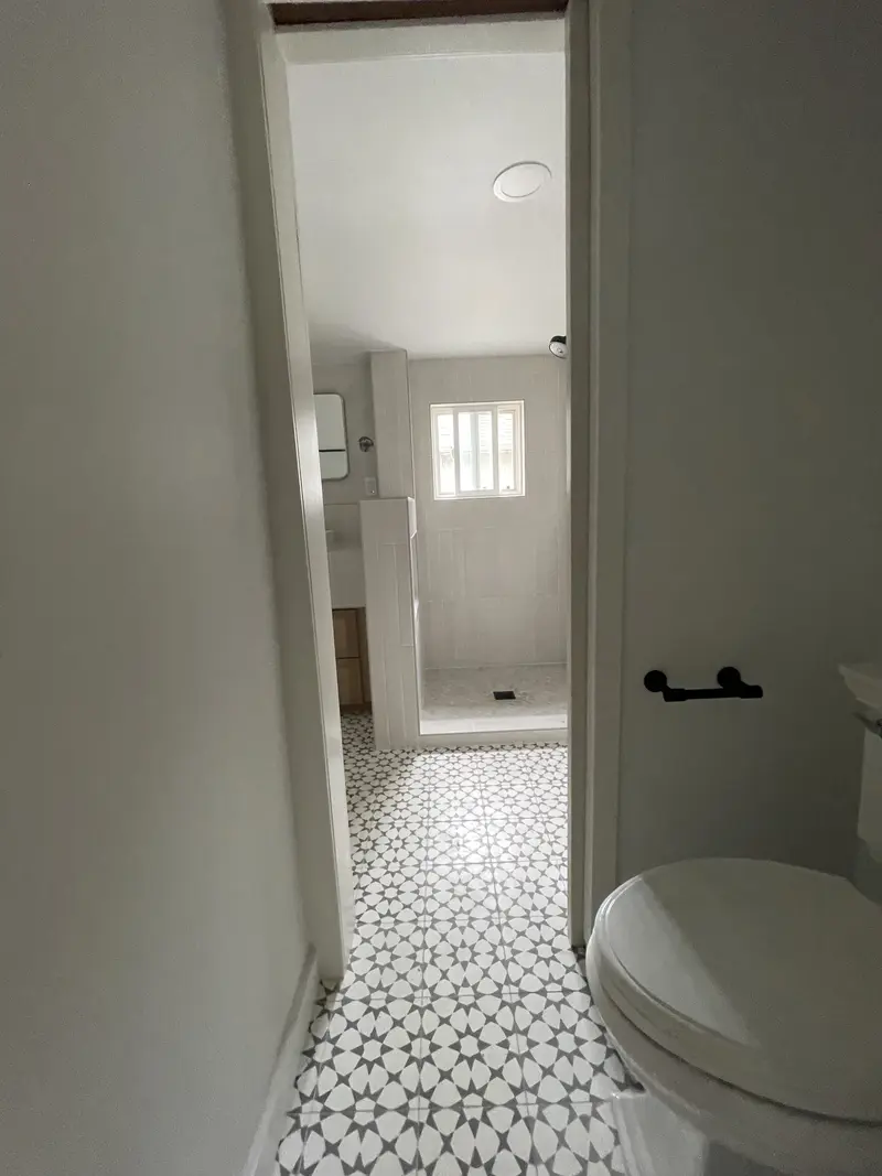 View through the bathroom doorway across a gray and white star pattern floor to the walk-in shower