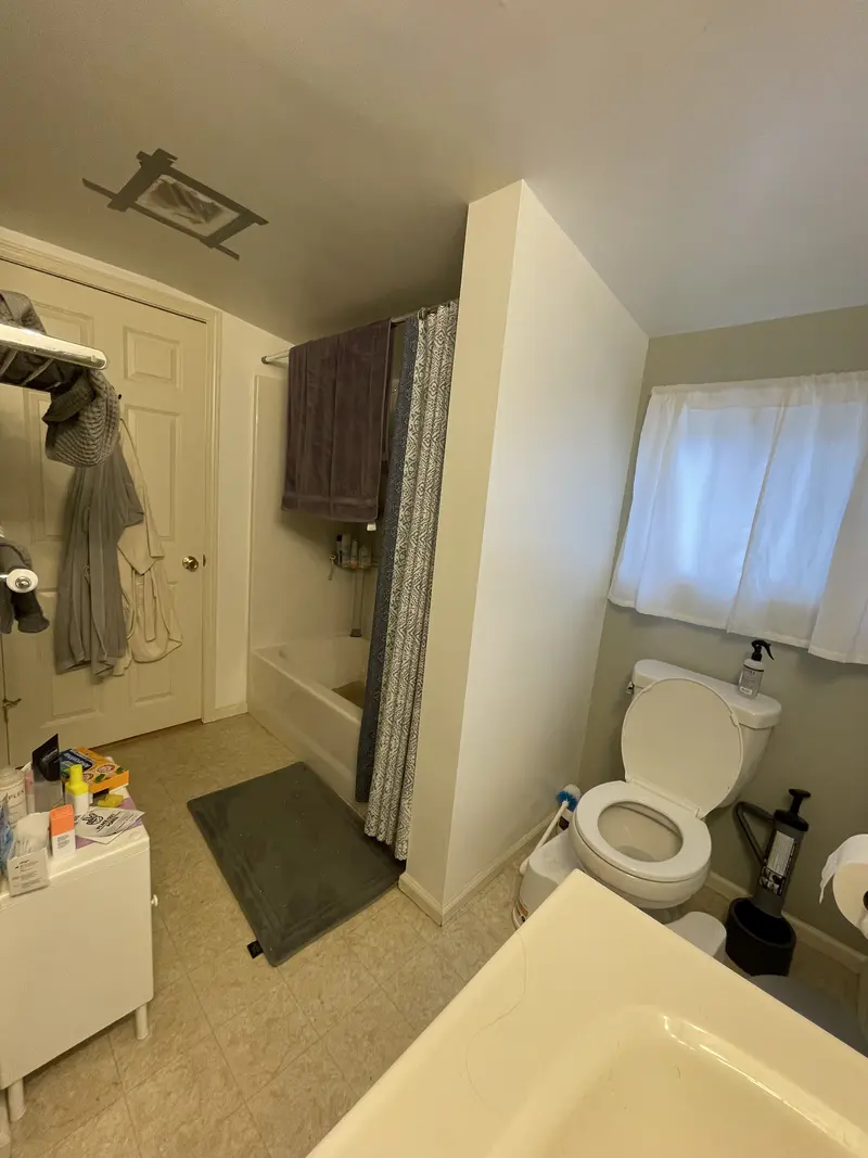 Old bathroom with a tub and curtain, a toilet under a curtained window and cluttered counters