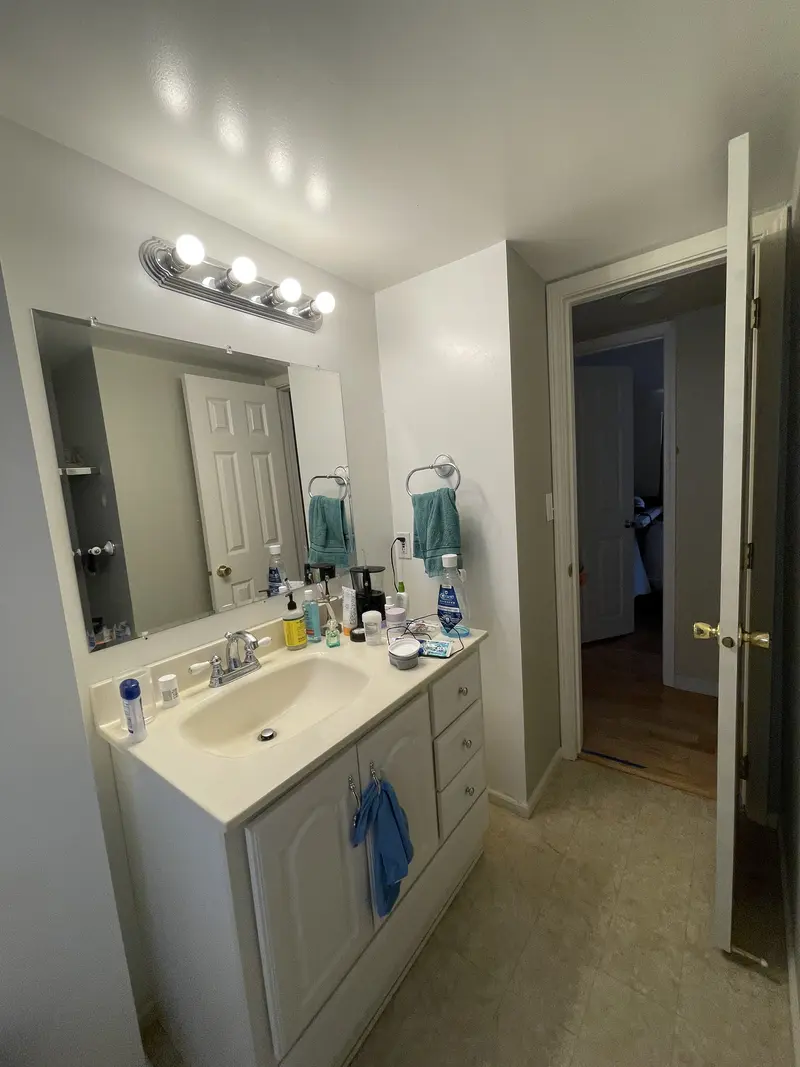 Bathroom before the remodel with a single white vanity, a mirror with bulb lights and a vinyl floor