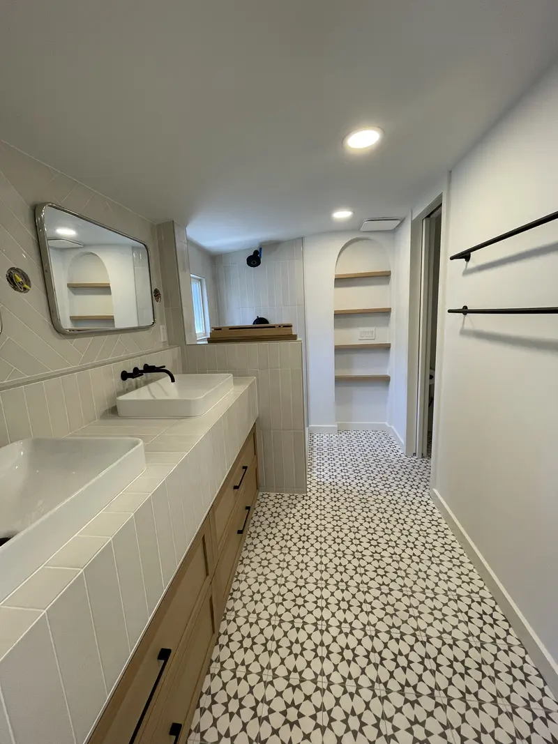 Long oak double vanity with white tiled top, two vessel sinks and black faucets over a star tile floor