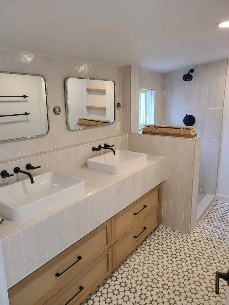 White tiled vanity top with two vessel sinks, black wall-mounted faucets and two mirrors