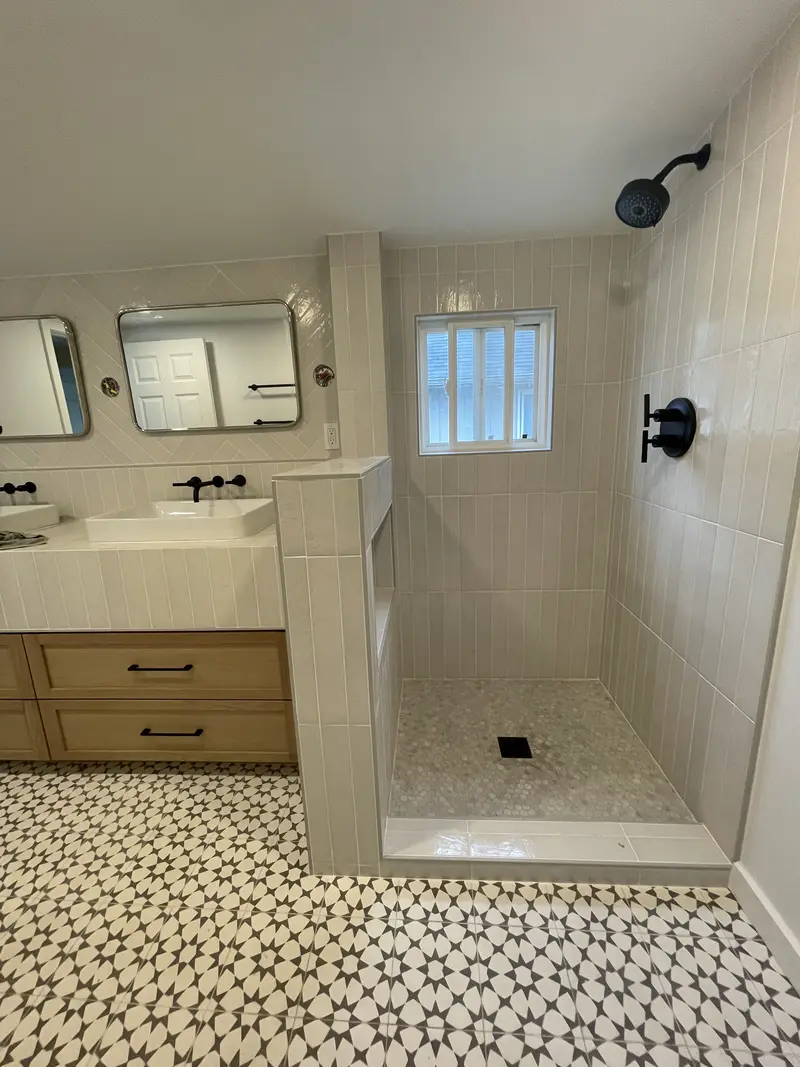 Walk-in shower with white vertical tile, a tiled half wall, a window and a matte black shower head beside a wood double vanity