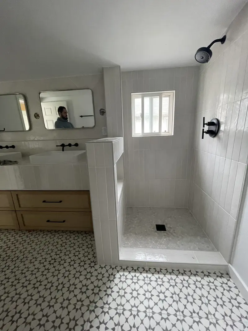 Walk-in shower behind a tiled half wall with a window and black shower head