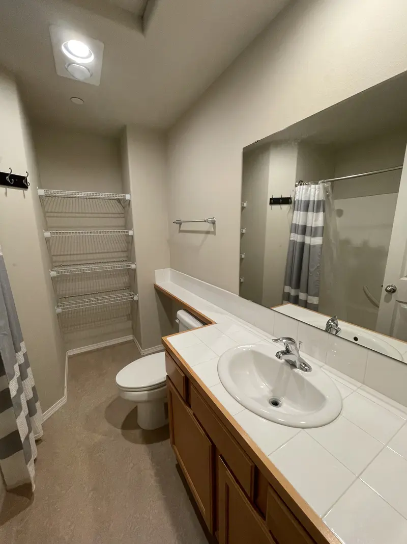 Old white tile counter with a drop-in sink, a large plain mirror and a striped shower curtain