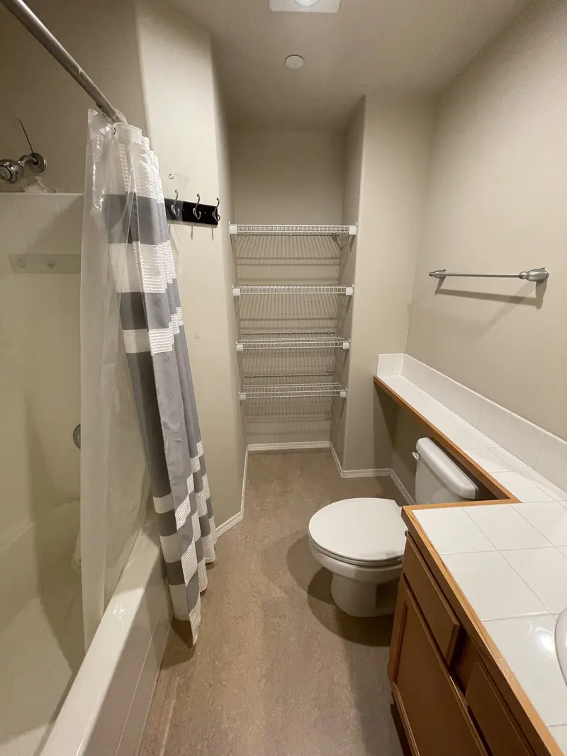 Old tub with a curtain rod, a toilet and wire shelving on the back wall