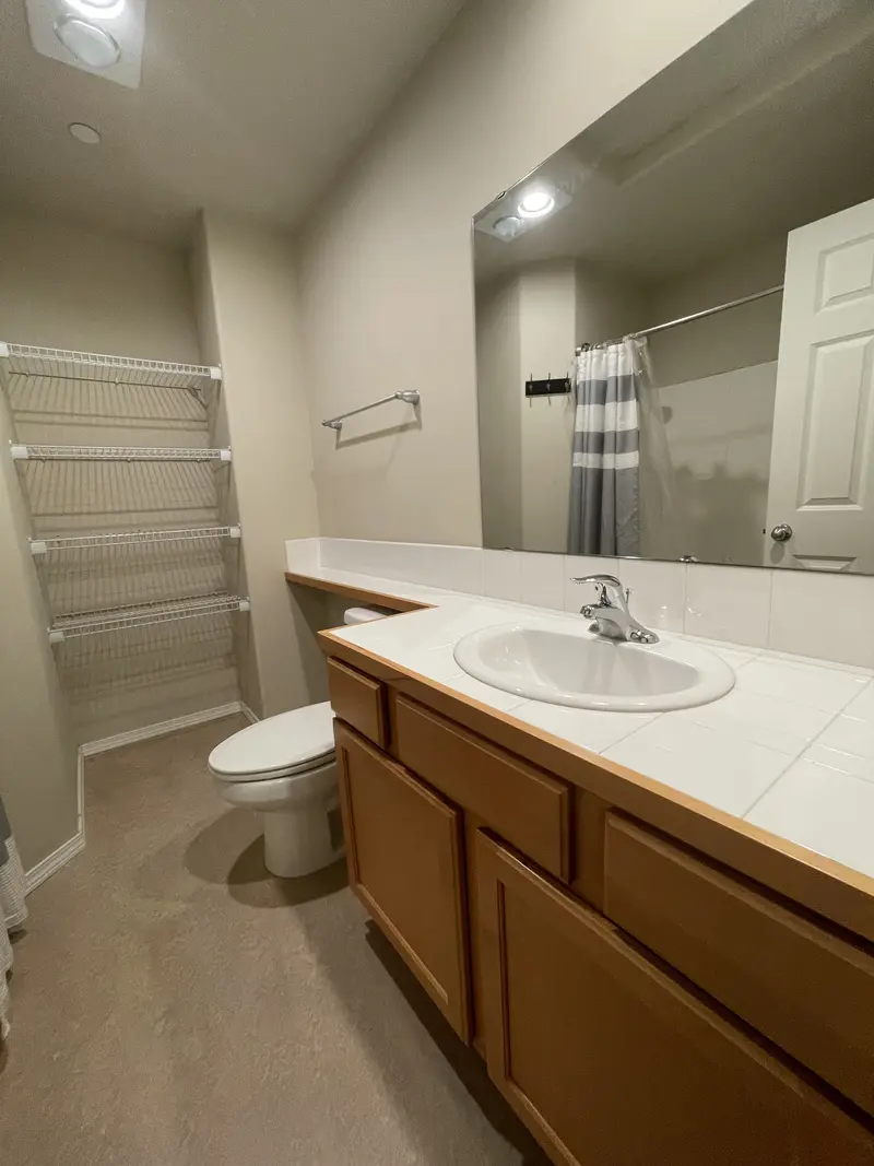 Bathroom before the remodel with a wood vanity and white tile counter, a toilet and wire shelving