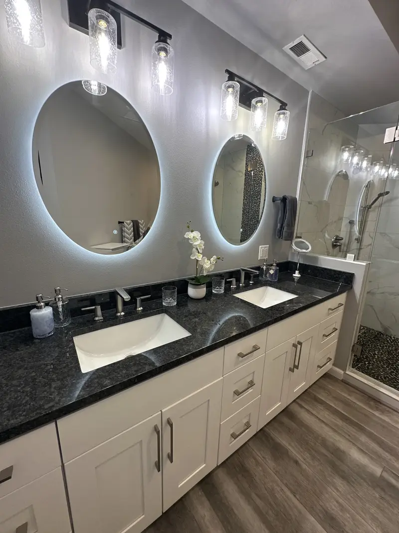 Close view of the dark speckled counter, undermount sink and lit oval mirror