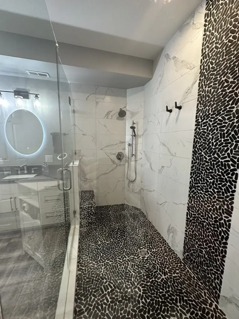 Frameless glass shower panel with the black pebble floor and marble-look tile inside