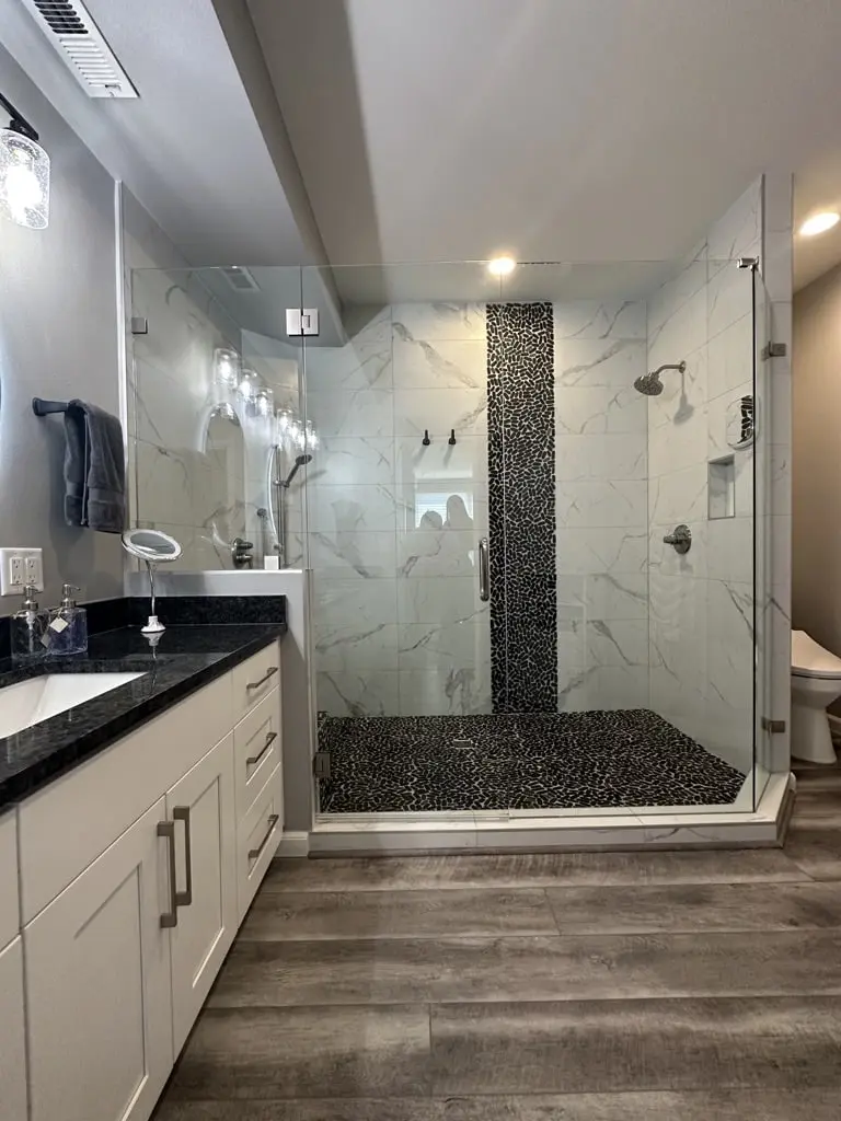 Vanity end with a dark counter beside the walk-in shower and its pebble stripe