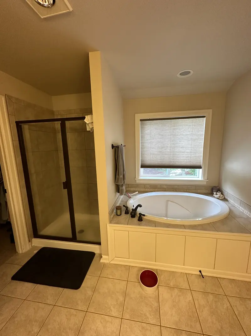 Primary bathroom before the remodel with a tiled corner tub under a window and a framed glass shower