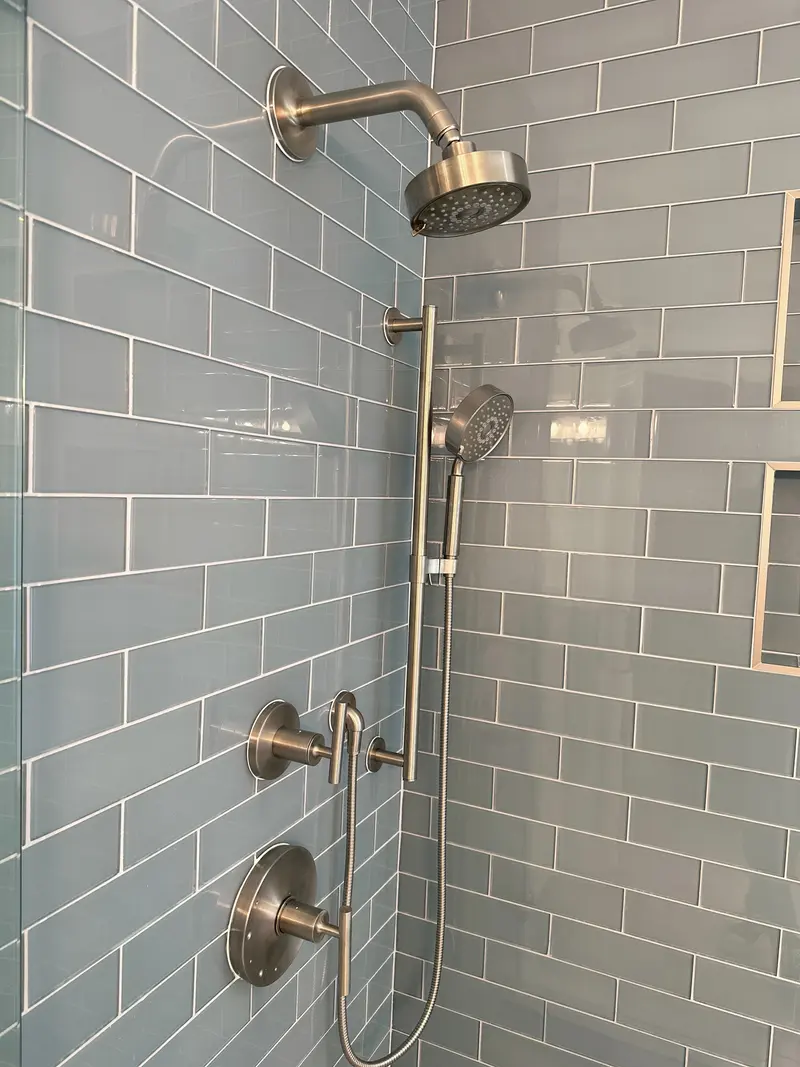 Brushed nickel rain head, handheld shower on a slide bar and two valves on blue glass subway tile