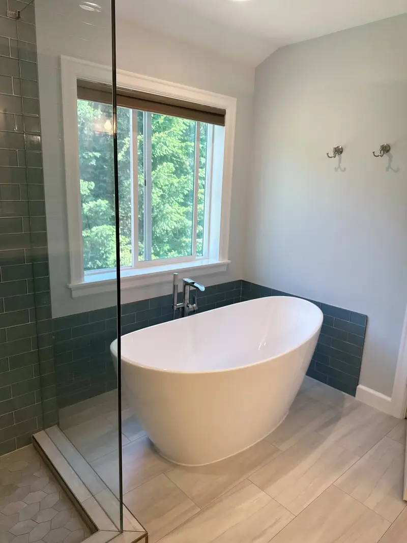 Freestanding tub with a deck-mounted filler under a window framed by dark tile wainscot