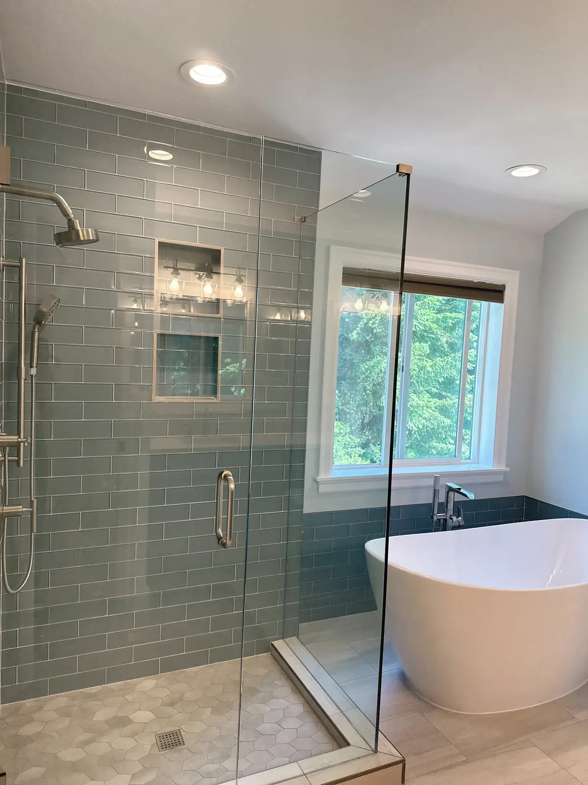 Frameless glass shower in blue glass subway tile with two niches beside a freestanding tub