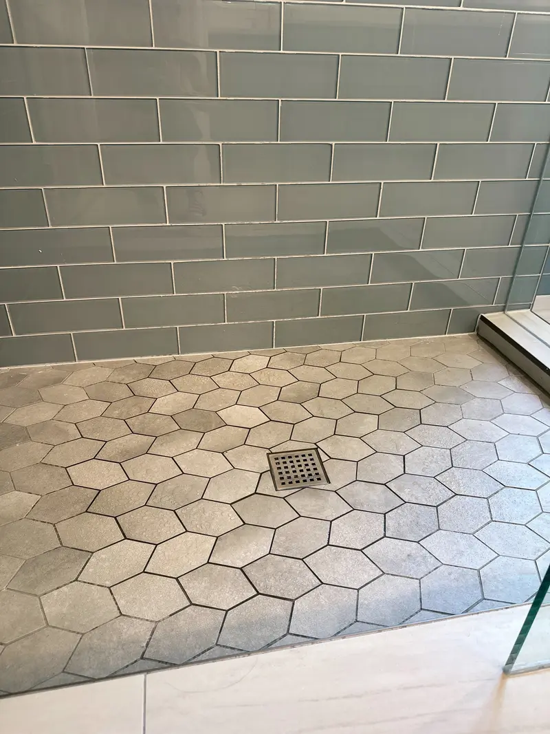 Gray hexagon tile shower floor around a square drain with blue glass subway tile walls